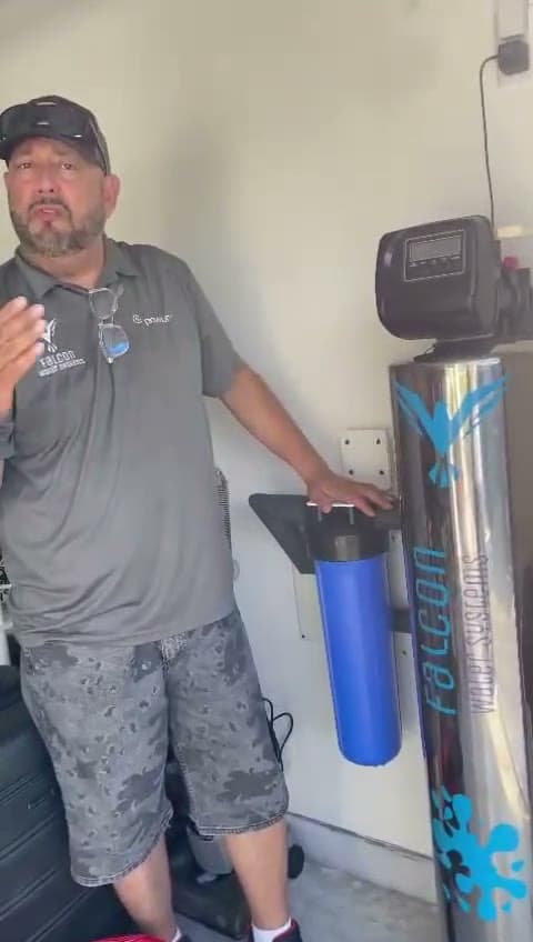 Noel Falcon showing a whole home water system and blue prefilter in a garage