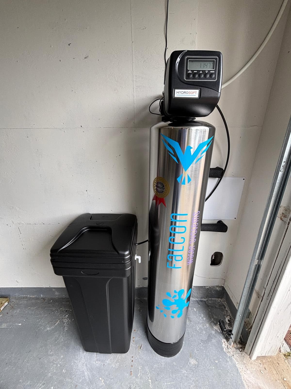 Stainless steel Falcon water softener with digital metered control valve, installed in a Houston garage